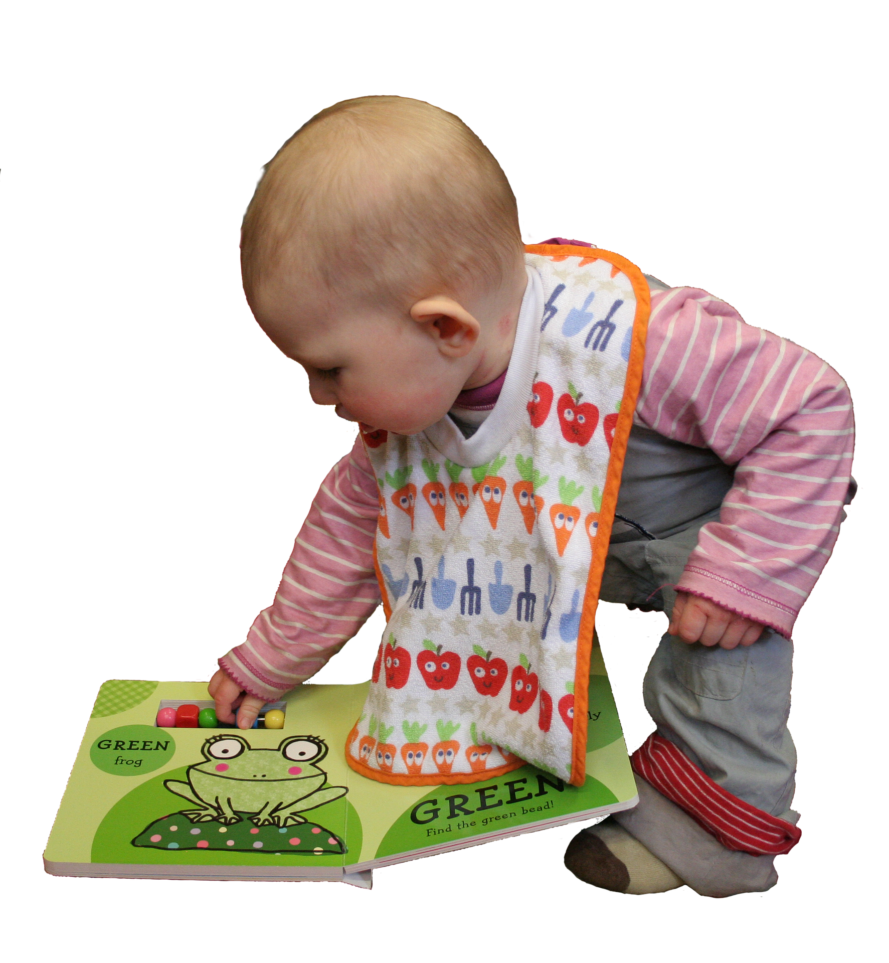 Image of baby in a pink top, gray pants, and orange bib leaning over and looking at a green book.