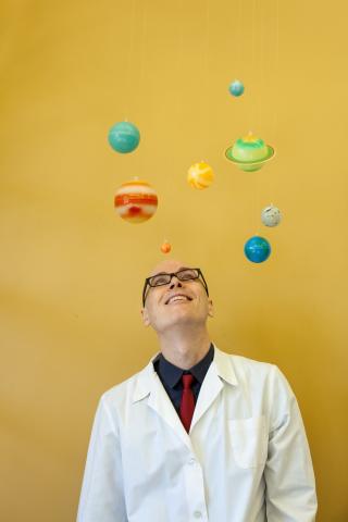 man in lab coat looking at planets on yellow background